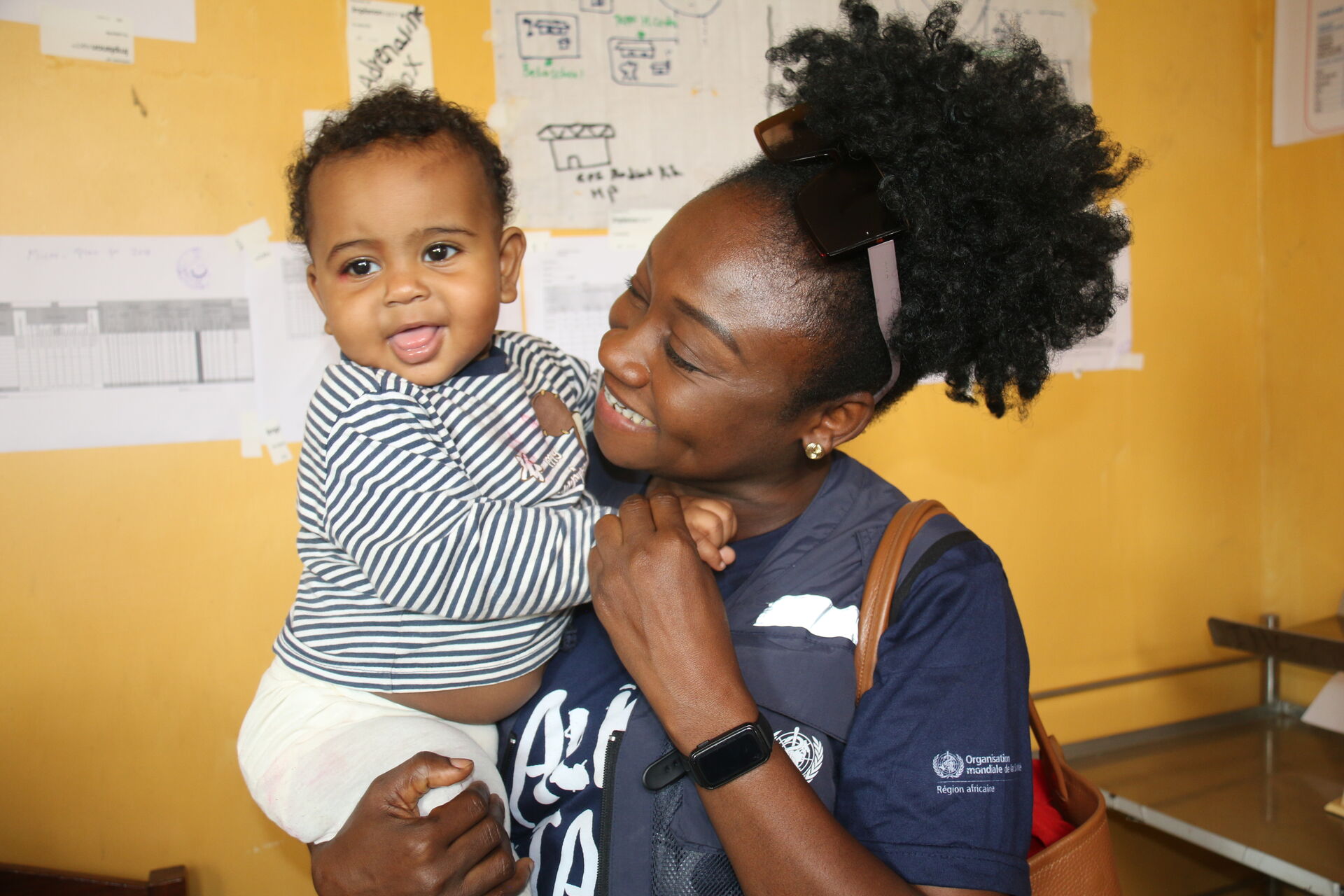 Woman in WHO vest holding smiling infant